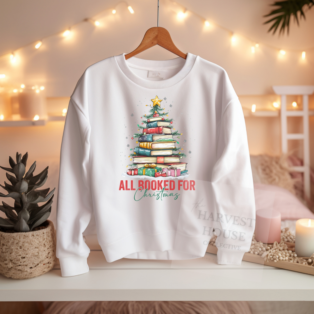 White sweatshirt with Christmas tree design and text on a hanger against a warm, decorated background.